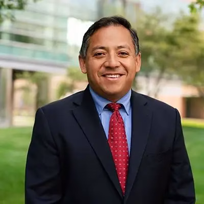 Dr. Carlos Franco-Paredes, infectious disease specialist and medical advisor, smiling in professional headshot wearing dark suit and red tie