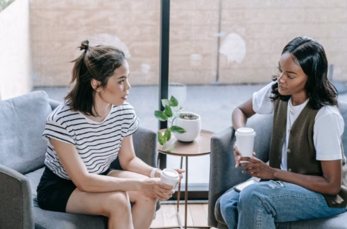Two women sitting across from each other having a supportive conversation in a comfortable living room setting