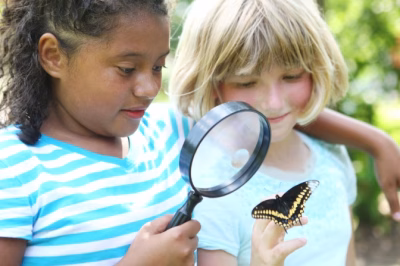 Two children examining a butterfly with a magnifying glass outdoors