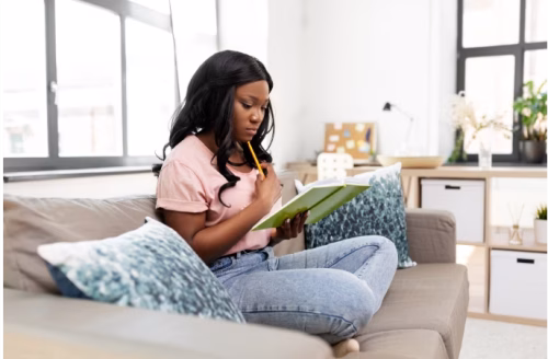 Person sitting cross-legged on couch reading a book in bright, naturally-lit living room