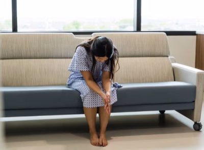 Person sitting on couch with head down and hands covering face, showing signs of sensory overload during emergency room visit