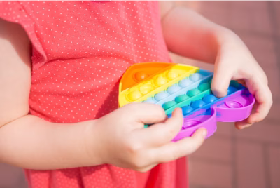 Child in coral shirt holding rainbow fidget toy with sensory bubbles in their hands