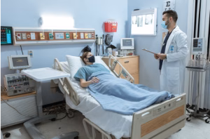 Hospital room with patient in bed speaking with doctor in white coat, medical equipment visible on walls
