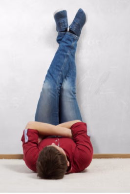 Person lying on floor with legs elevated against a wall, wearing red shirt and jeans, demonstrating position to help with low blood pressure