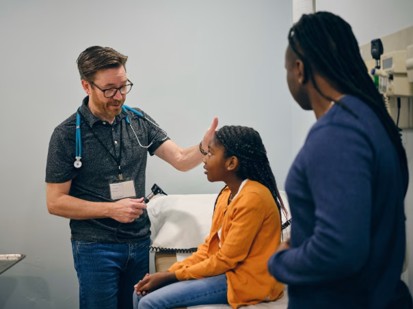 Healthcare provider speaking with patient and support person in exam room, demonstrating communication during an emergency room visit