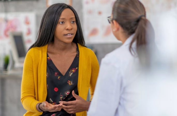 Patient in yellow cardigan speaking with healthcare provider in white coat during medical appointment about treatment concerns