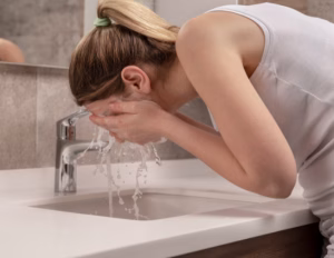 Person leaning over bathroom sink splashing cold water on their face